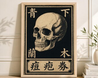 May include: Framed art print featuring a detailed illustration of a human skull against a black background. The skull is rendered in shades of beige and tan, with Japanese characters above and below. The frame is a light wood color.