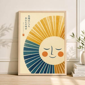 May include: Framed art print featuring a smiling sun with closed eyes, rendered in yellow, blue, and orange hues. The sun's rays radiate outwards. Japanese text is visible in the upper left corner. The artwork is in a light wood frame.