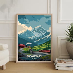 May include: A framed art print showing a stylized landscape of Skagway, Alaska. The artwork depicts a red train winding through a green valley, with snow-capped mountains in the background under a blue sky. The word "SKAGWAY" is printed at the bottom.