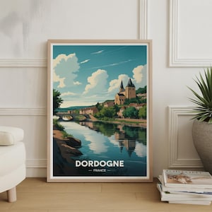 May include: Framed art print featuring a scenic view of the Dordogne region in France. The artwork depicts a river with a bridge, buildings, and a church under a blue sky with clouds. The word "DORDOGNE" is printed at the bottom.
