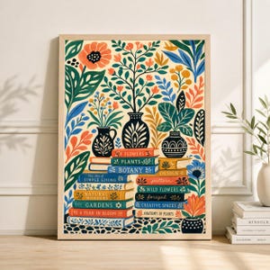 May include: A framed botanical art print featuring a stack of books with titles like "Flowers," "Botany," and "Gardens." The artwork showcases colorful illustrations of flowers, plants, and vases in shades of orange, blue, and green, creating a vibrant and decorative piece.