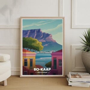Peut inclure: Impression d'art encadrée représentant une illustration colorée de Bo-Kaap, Afrique du Sud. L'œuvre représente des bâtiments vibrants, une chaîne de montagnes et le texte "BO-KAAP - SOUTH AFRICA". L'impression est dans un cadre en bois clair.
