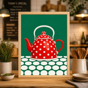 Op de afbeelding: Een ingelijste print met een rode theepot met witte stippen. De theepot heeft een witte handgreep en tuit, tegen een groene achtergrond. De basis van de theepot staat op een wit en groen patroon. De lijst is lichtbruin.
