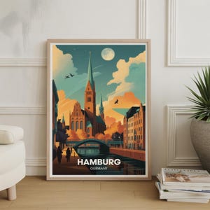 May include: A framed art print featuring a stylized illustration of Hamburg, Germany. The artwork depicts a church with a tall spire, a bridge, and buildings along a canal, under a sky with a full moon and birds. The word "HAMBURG" is displayed.