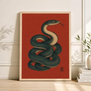 May include: A framed art print showing a coiled snake illustration. The snake is teal and cream against a red backdrop. The artwork has a vintage aesthetic, with a wooden frame.