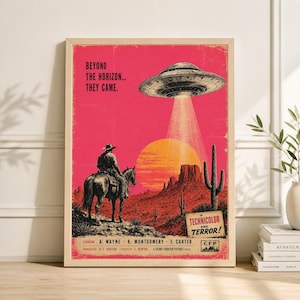 May include: A framed vintage-style poster with a retro sci-fi theme. The poster features a cowboy on horseback, a UFO, and desert scenery in shades of red, orange, and brown. Text includes "Beyond the Horizon... They Came."