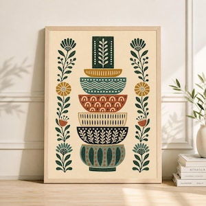 May include: A framed art print featuring a stack of decorative bowls in various colors and patterns. The bowls are arranged vertically, with floral and leaf motifs on either side. The color palette includes green, brown, and red.