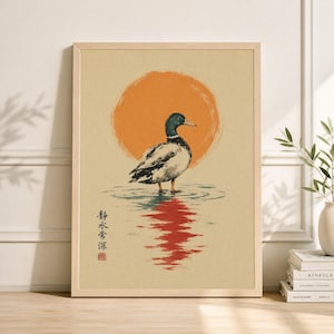 May include: Framed art print featuring a duck standing in water with an orange sun in the background. The duck has a green head and white and black body. The water reflects the sun's light. The print has Japanese text.