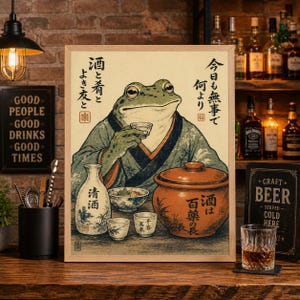 Puede incluir: Un grabado enmarcado que presenta una rana con vestimenta tradicional japonesa, sosteniendo una taza de sake. La obra de arte incluye texto japonés e imágenes de botellas, cuencos y tazas de sake, con una paleta de colores cálidos. El grabado se muestra sobre una superficie de madera.