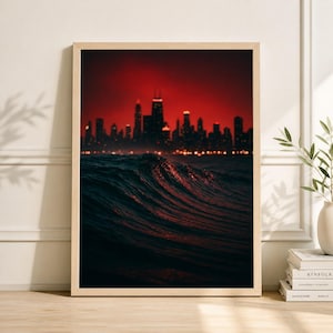 May include: Framed art print depicting a dark seascape with a city skyline. The image shows a wave in the foreground, with city lights reflecting on the water. The sky is a deep red, creating a dramatic contrast.