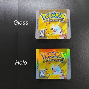 May include: Two gold-colored Pokemon game cartridge labels with a yellow Pikachu character. The top label is a gloss finish and the bottom label is a holographic finish. Both labels have the text "Pokemon Special Pikachu Edition" and "This Side Out".