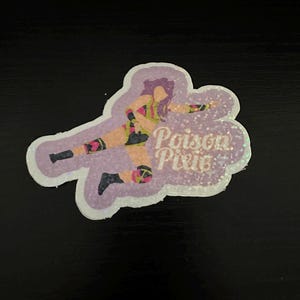 Puede incluir: Una pegatina de purpurina morada, verde y rosa con una imagen de dibujos animados de una mujer en una pose de lucha. El texto "Poison Pixie" está escrito en purpurina blanca.