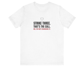 May include: A white short-sleeve t-shirt featuring a black outline of a home plate icon above the black text STRIKE THREE. THAT'S THE CALL. and the red text NO, I'M NOT CHANGING IT. centered on the chest of the garment.