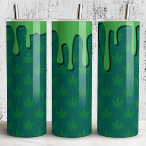Puede incluir: Tres vasos altos y cilíndricos con un patrón de hojas de cannabis verdes. La parte superior de cada vaso tiene un diseño de pintura verde goteando con contornos negros. Cada vaso tiene una pajita plateada.
