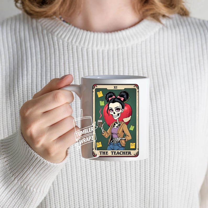 May include: White ceramic mug featuring a tarot card design with a skeleton teacher illustration. The card reads "THE TEACHER" and includes a red apple, coffee, and sticky notes. The mug is held by a person wearing a white sweater.