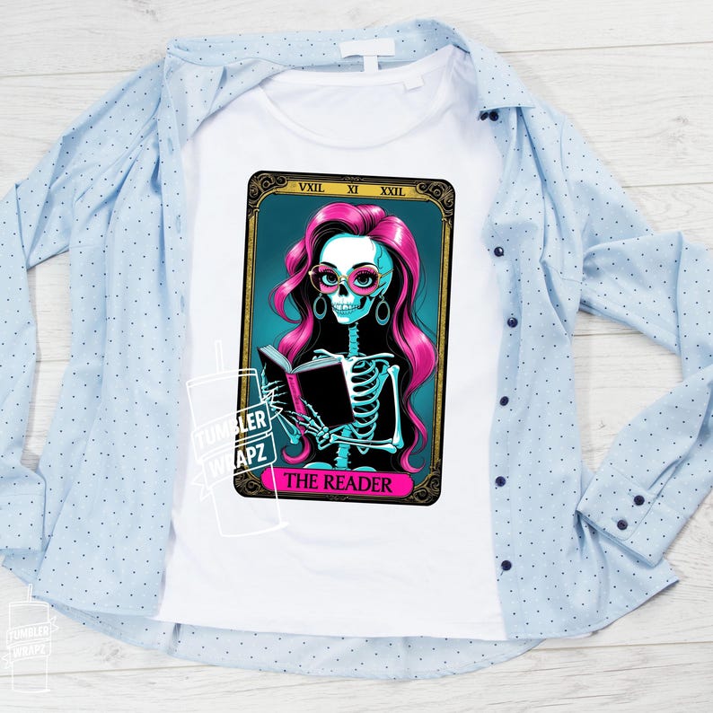 May include: White t-shirt featuring a tarot card design with a skeleton reading a book. The skeleton has pink hair, glasses, and earrings. The card reads "THE READER" in pink text. A light blue button-down shirt is draped over the t-shirt.