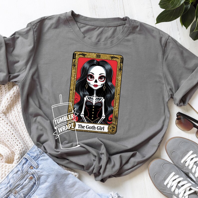 May include: Gray t-shirt featuring a tarot card design with a skeleton woman with long black hair, red lips, and a black corset. The card is framed in gold with the text "The Goth Girl".