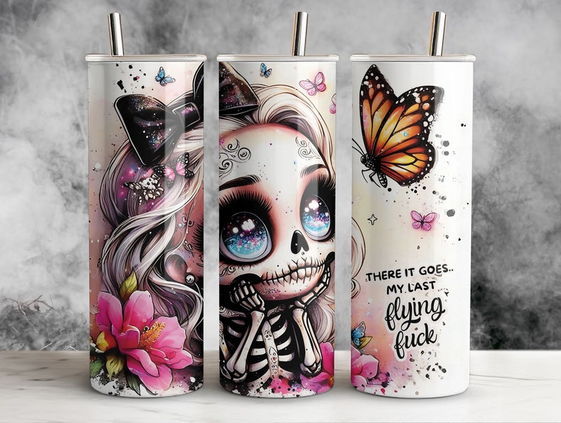 May include: Three stainless steel tumblers with different designs. The first tumbler features a pink flower and a skull with a bow. The second tumbler features a skull with a bow and blue eyes. The third tumbler features a butterfly and the text "There it goes... My last flying f***".