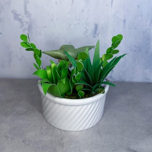 Op de afbeelding: Een witte keramische pot met een groene succulent plant en een klein groen beeldje erin. De pot heeft een swirl-ontwerp.