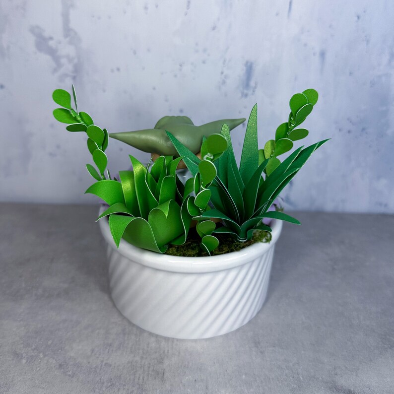 Op de afbeelding: Een witte keramische pot met een groene succulent plant en een klein groen beeldje erin. De pot heeft een swirl-ontwerp.