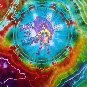 May include: A tie-dye t-shirt featuring a vibrant, multi-colored spiral pattern in red, orange, yellow, green, and blue. In the center, a graphic depicts a figure holding an umbrella with the text "BOX OF RAIN" printed in purple block letters.