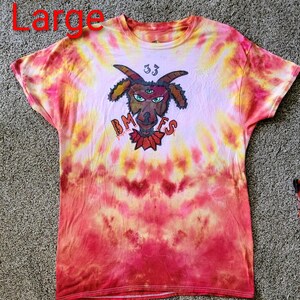 May include: A tie-dye t-shirt in shades of pink, yellow, and red. The shirt features a graphic of a goat with three eyes, the number 33, and the letters "BMFES". The word "Large" is visible in the top left corner.
