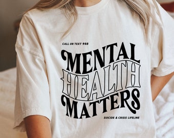 May include: White t-shirt with black text that reads "Call or Text 988" and "Mental Health Matters" with the text "Suicide & Crisis Lifeline" below.