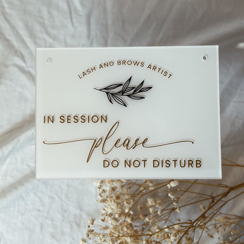 May include: White acrylic sign with gold lettering that reads "Lash and Brows Artist" and "In Session Please Do Not Disturb". A small black twig design is above the text.