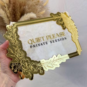 May include: A gold-colored sign with the words "QUIET PLEASE PRIVATE SESSION" in gold lettering. The sign has a decorative floral border and a white background.