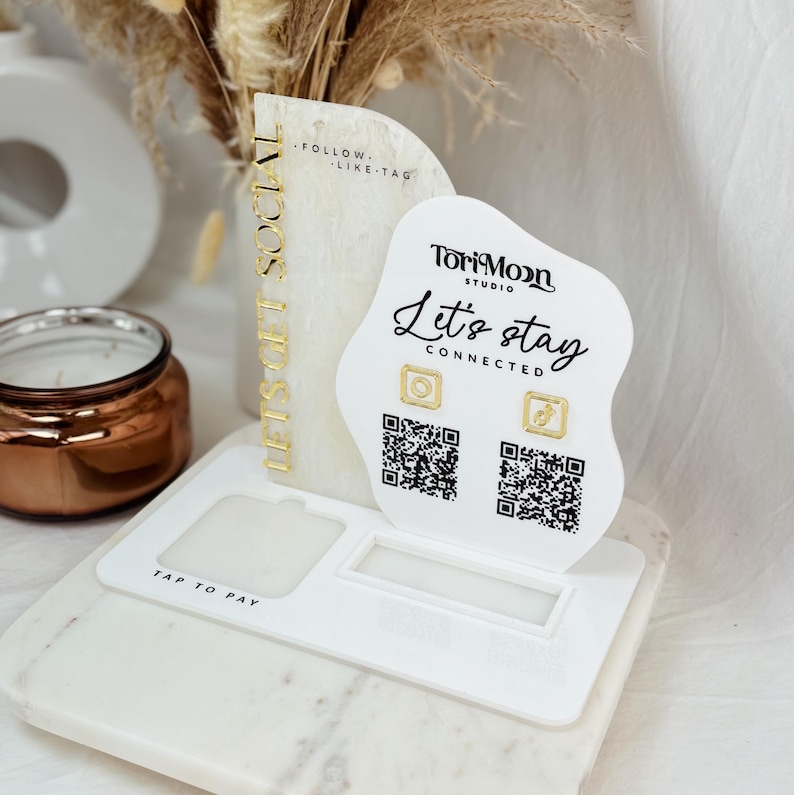 Peut inclure: Un pr&eacute;sentoir blanc avec le texte "Let's stay connected" et le logo ToriMoon Studio. Le pr&eacute;sentoir comporte deux codes QR et deux ic&ocirc;nes dor&eacute;es, l'une d'un appareil photo et l'autre d'un &eacute;clair. Le pr&eacute;sentoir est pos&eacute; sur une surface en marbre blanc. Le texte "Follow, Like, Tag" est sur le c&ocirc;t&eacute; gauche du pr&eacute;sentoir. Le texte "Tap to Pay" est sur le c&ocirc;t&eacute; inf&eacute;rieur droit du pr&eacute;sentoir.