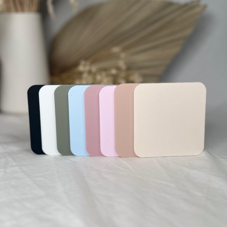 May include: Six square-shaped coasters in different colors: black, white, gray, light blue, pink, and beige.