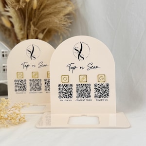 May include: Two beige acrylic display stands with arched tops. Each stand features a logo, the text "Tap n Scan", and three QR codes with corresponding text: "Follow Us", "Consent Form", and "Review Us".