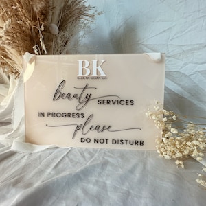 May include: A pink acrylic sign with black text that reads "BK Hair by Bobby Kay beauty services in progress please do not disturb".