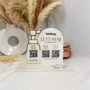 May include: A decorative acrylic display with a pump bottle design and the text "SCAN ME!". It also features a curved sign with "LET'S STAY CONNECTED" and social media icons. The base reads "your BEAUTY JOURNEY starts here."