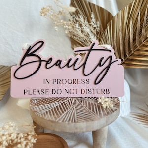 May include: Pink wooden sign with the text "Beauty in progress, please do not disturb" in black lettering.