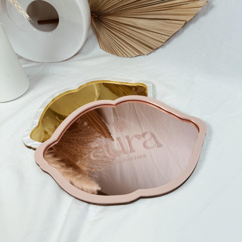May include: Two pink and gold cloud-shaped decorative mirrors with the word "aura" embossed on the pink mirror.