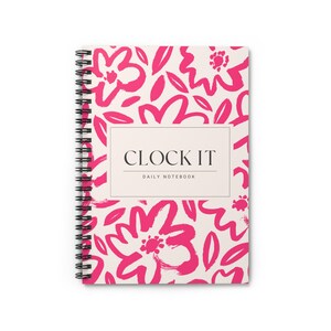 Op de afbeelding: Een spiraalgebonden notitieboek met een crèmekleurige kaft met een levendig roze bloemenpatroon. De tekst "CLOCK IT" staat in een rechthoekig kader, met daaronder "DAILY NOTEBOOK". De binding van het notitieboek is zwart.