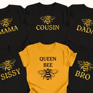 May include: Six black t-shirts with gold text and bee illustrations. The shirts say "Mama", "Cousin", "Dada", "Sissy", "Bro", and "Queen Bee".