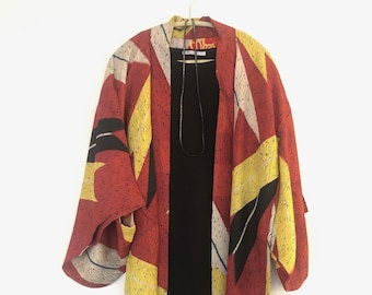 May include: A red, yellow, and white patterned kimono with a black long-sleeved shirt underneath.