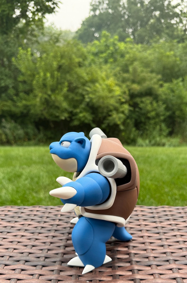 May include: A blue and brown bipedal creature figurine with a turtle-like shell, featuring two grey cylindrical cannons protruding from the back, a cream-colored underbelly, and sharp white claws on the hands and feet, captured in profile.