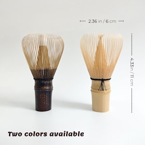 May include: Two bamboo matcha whisks, 11 cm tall and 6 cm wide, in two colours. One whisk has a dark brown handle, the other a light beige handle. The text "Two colours available" is at the bottom.