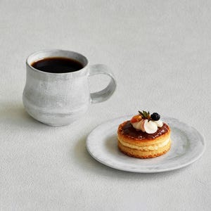 K&ouml;nnte beinhalten: Ein Set aus drei Keramikbechern mit gesprenkelter, matter Oberfl&auml;che. Die Becher sind in Creme-, Hellgrau- und Dunkelgraut&ouml;nen gehalten. Jeder Becher hat ein schlichtes, minimalistisches Design und einen abgerundeten Henkel.