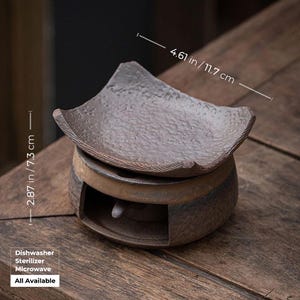 May include: A brown ceramic tea warmer with a textured, square top, measuring 4.61 inches (11.7 cm) wide. The base has a circular design with an opening. The text "Dishwasher Sterilizer Microwave All Available" is visible.