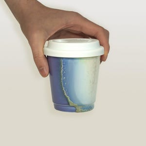 May include: A purple and blue ceramic reusable coffee cup with a white lid. The cup has a unique marbled design.