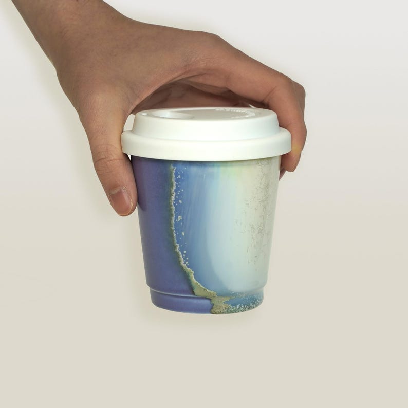 May include: A purple and blue ceramic reusable coffee cup with a white lid. The cup has a unique marbled design.