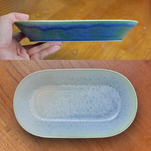May include: A ceramic serving dish with a rectangular shape and rounded edges. The dish has a speckled, light blue interior and a gradient of blue and green on the exterior. The dish is held in a hand.