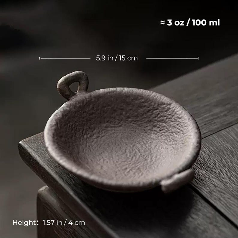 May include: A small, dark brown ceramic bowl with a handle. The bowl is approximately 5.9 inches (15 cm) in diameter and 1.57 inches (4 cm) high, with a capacity of about 3 oz (100 ml). The bowl has a textured surface and is designed for serving.