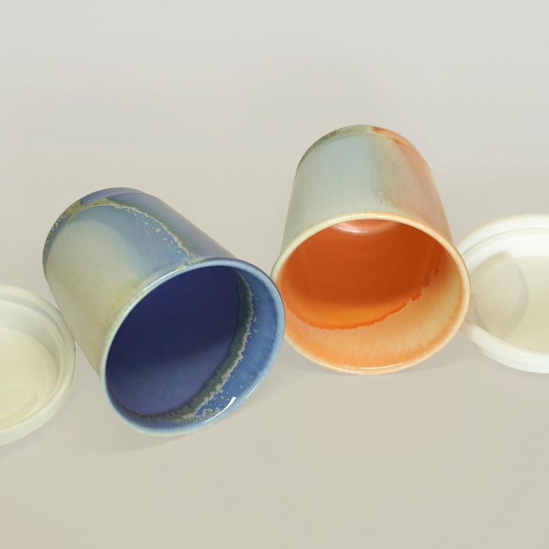 May include: Three ceramic mugs with lids. The mugs are in shades of blue, orange, and white. The lids are white.