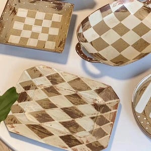 May include: A collection of handmade ceramic serving dishes with a checkerboard pattern in shades of brown and cream. The set includes a square plate, a cup with a handle, a rectangular platter, and a round plate.