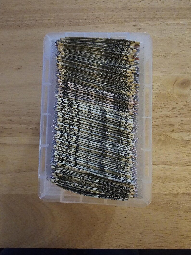 May include: A clear plastic storage container filled with a stack of folded dollar bills.